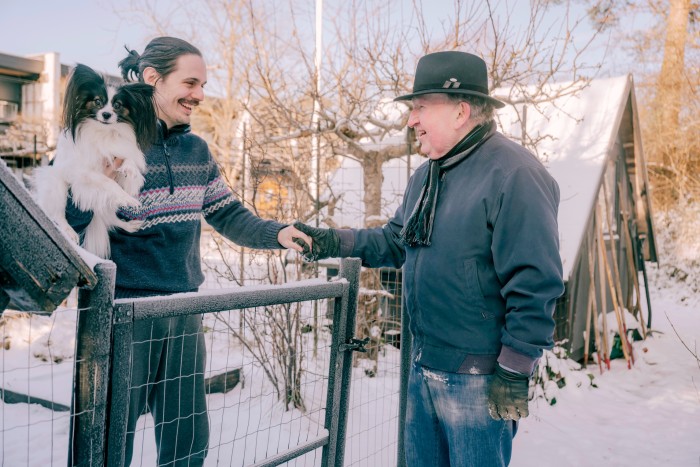 Morten and his neighbour holding a Papillon dog chat over a fence in a snowy landscape 