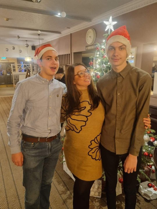 Kellie Whitehead with her two sons (they're both wearing Santa hats) at Christmas, with a Christmas tree in the background