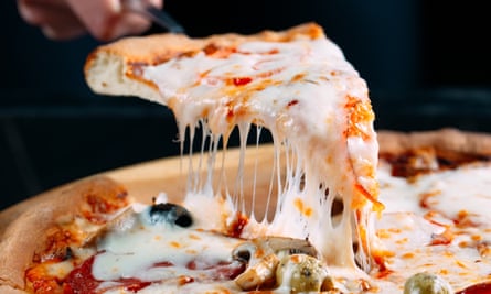 A hand lifting a slice of pizza that has a lot of cheese on it