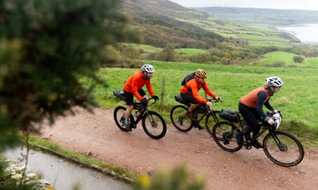 Adventure cyclists Mark Beaumont, Markus Stitz and Jenny Graham on gravel path near sea