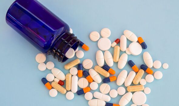 A pile of pills of different sizes, forms and colors on a pastel blue background coming out of a blue jar