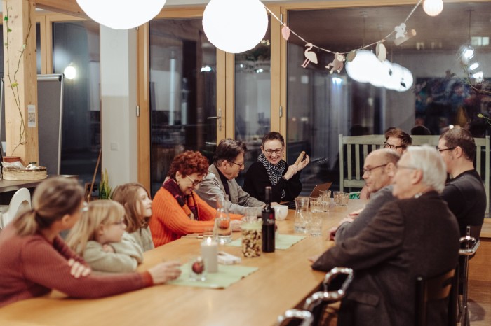 A group of adults and children chat around a long wooden table