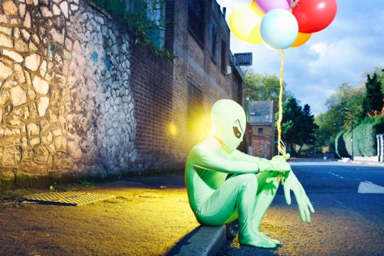 alien sitting in street with balloons