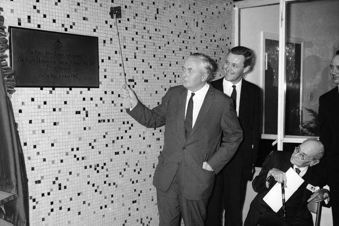 Prime Minister Harold Wilson unveils a plaque commemorating the opening of the then-named Post Office Tower in London on October 8 1965, watched by postmaster general Anthony Wedgwood Benn and Earl Clement Attlee