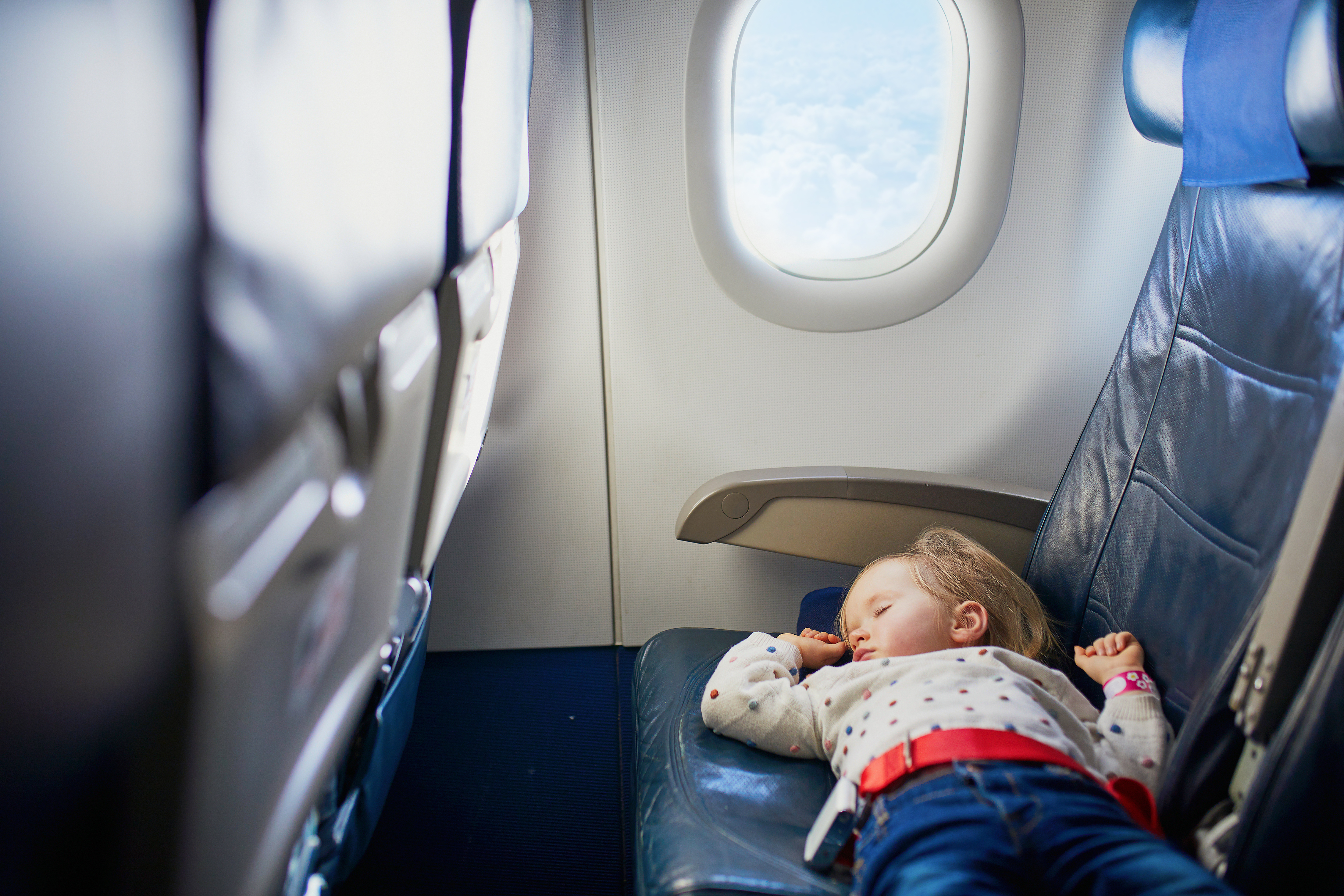 Adorable little toddler girl traveling by plane. Small child lying on a seat and sleeping during the flight. Traveling abroad with kids. Unaccompanied minor concept