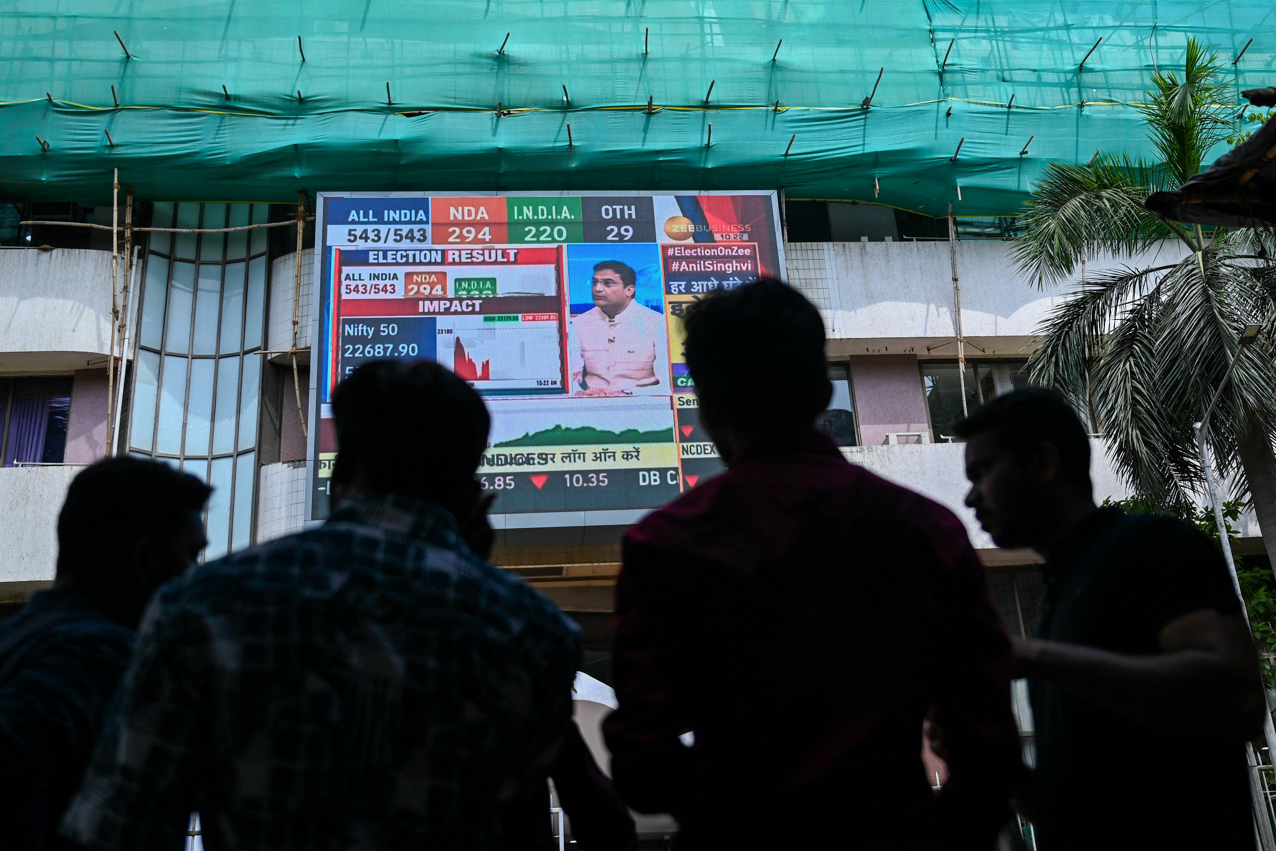 Pedestrians watch share prices on a digital broadcast outside the Bombay Stock Exchange