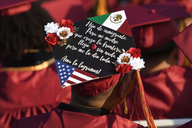 A graduate’s decorated cap says, “Son of an immigrant. For...