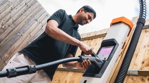 Nyobolt Sai Shivareddy smiling, in a black polo shirt, plugging in the charging cable for the new car