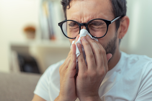 Young man sneezing, wiping his nose with a piece of tissue paper