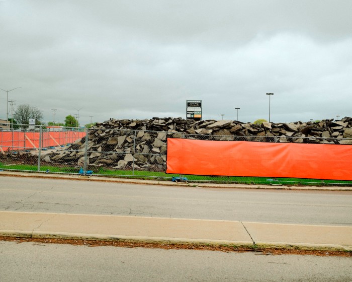 A wire fence with orange covering surrounds a site where there is a large mound of rubble