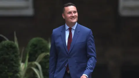 EPA Wes Streeting smiling as he walks down a street.