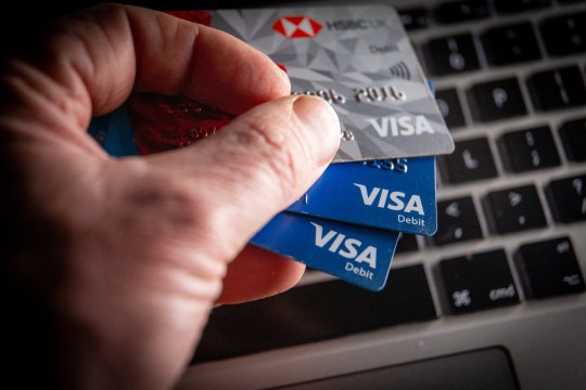 A hand holding three Visa cards above a keyboard.