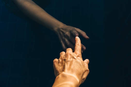 A stock image of a hand reaching out to touch another, shadowy, hand