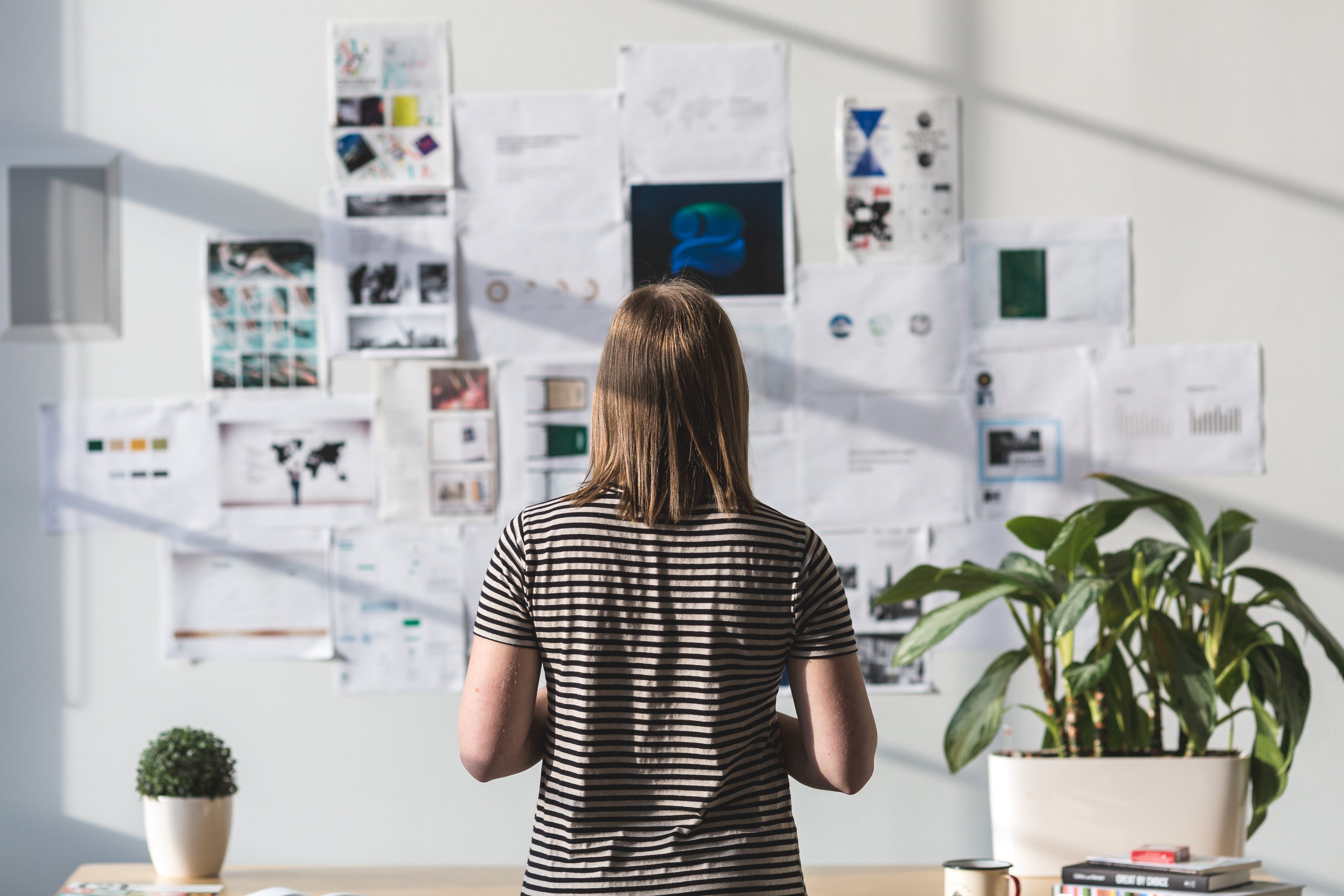 A person considers creative business ideas pinned to a wall.