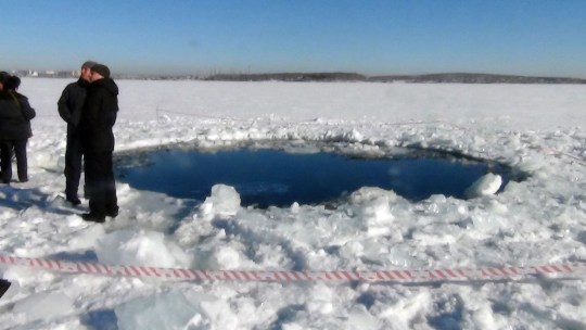 People standing near a six-metre hole in the ice of a frozen lake, reportedly the site of a meteor fall, outside the town of Chebakul in the Chelyabinsk region