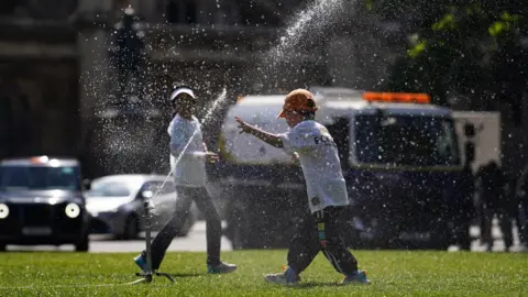 Jordan Pettitt/PA Wire Children run through a sprinkler on Parliament Square in London,