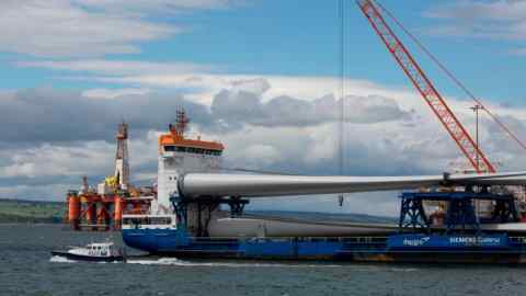 An oil and gas platform sits in the Moray Firth behind a ship carrying Wind turbine components