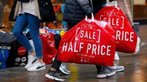 Pedestrians carrying Next branded shopping bags