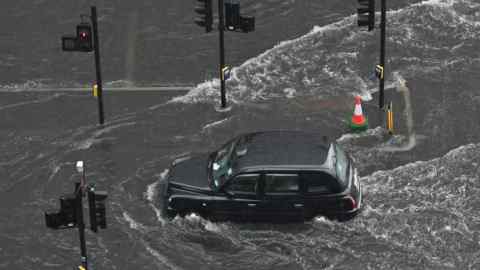 A taxi drives through a flooded road in London