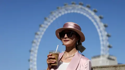 Reuters A woman holds a drink while posing for a photo in front of the London Eye, in London