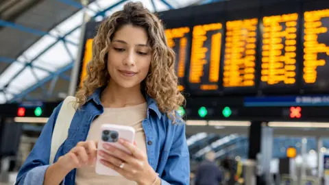 Getty Images Woman buying ticket on phone at train station