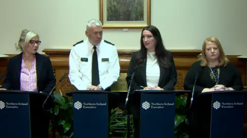 Michelle O'Neill, Jon Boutcher, Emma Little Pengelly and Naomi Long. They are standing behind podiums.