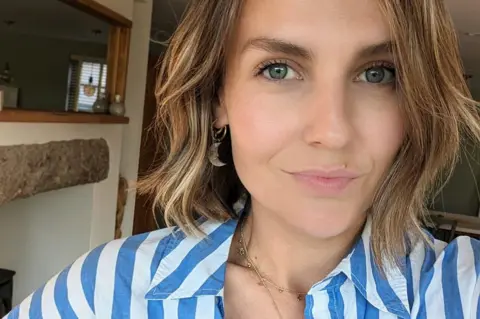 Olivia Lott Olivia Lott, a 30-year-old woman, takes a selfie indoors while looking at the camera and wearing a striped blue and white shirt