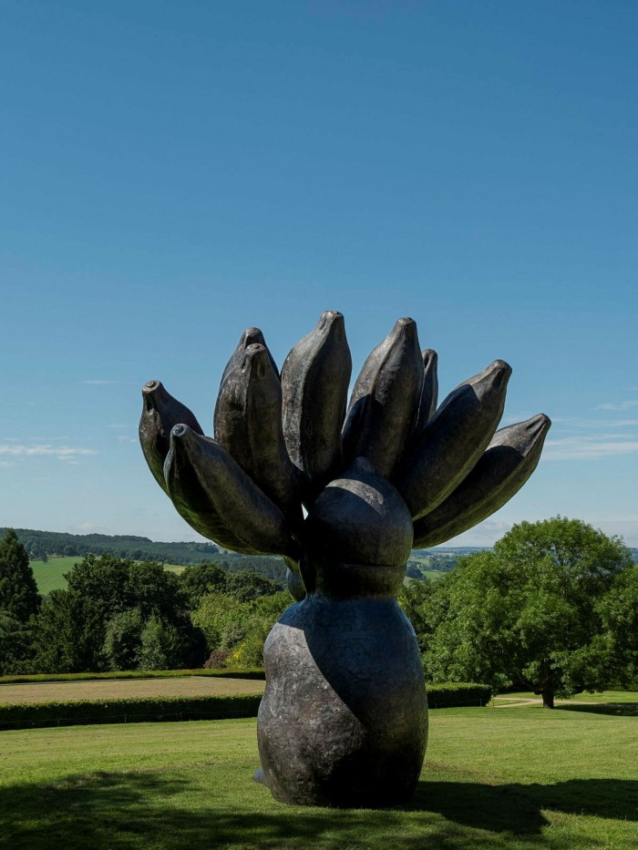 A large sculpture of a human-like figure with a bunch of bananas sprouting out of its head stands at the top of a hill 