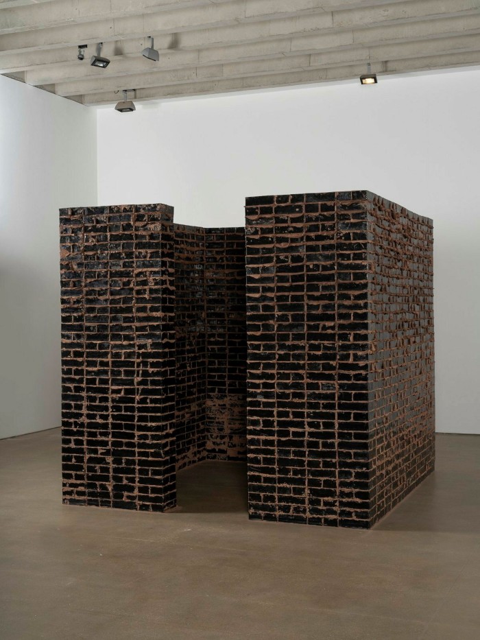 A square chamber inside an art gallery built from black bricks with an open entrance 