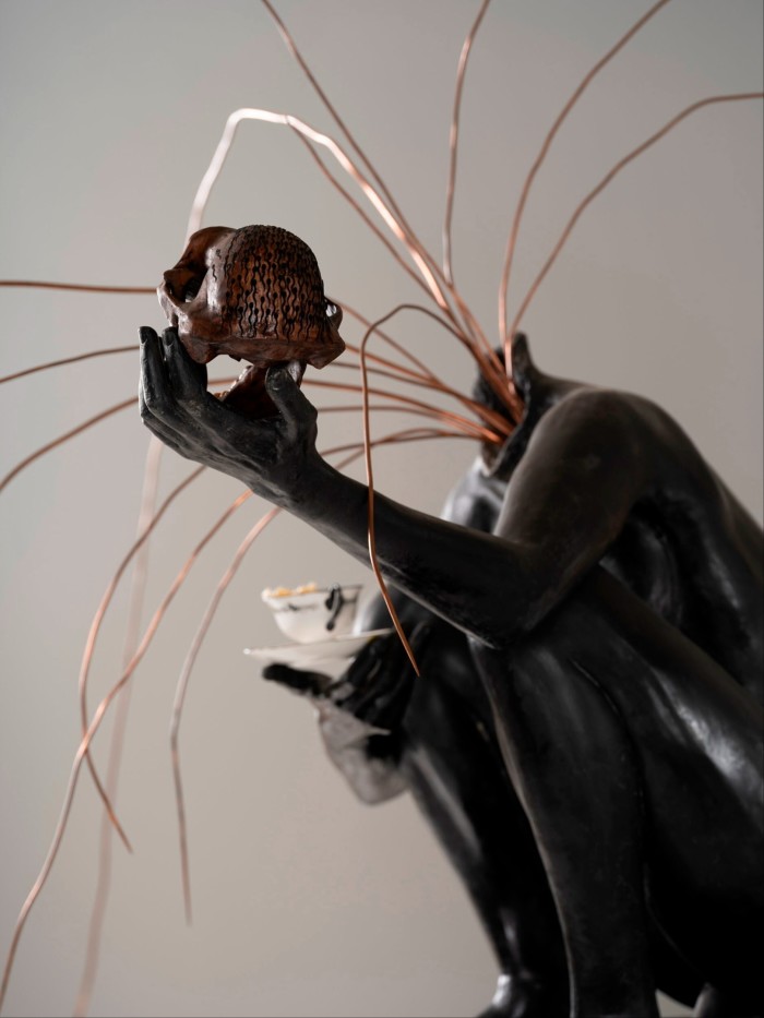 A statue of a woman holding a skull in her palm while wires spurt from her decapitated head