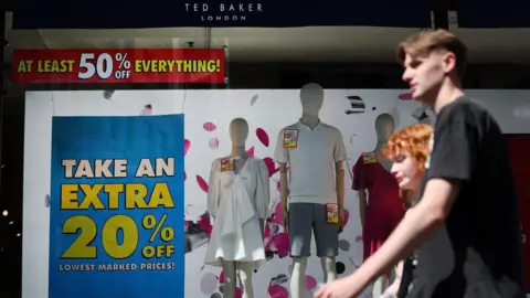 EPA Couple walking past a Ted Baker store with clearance sale signs in the window