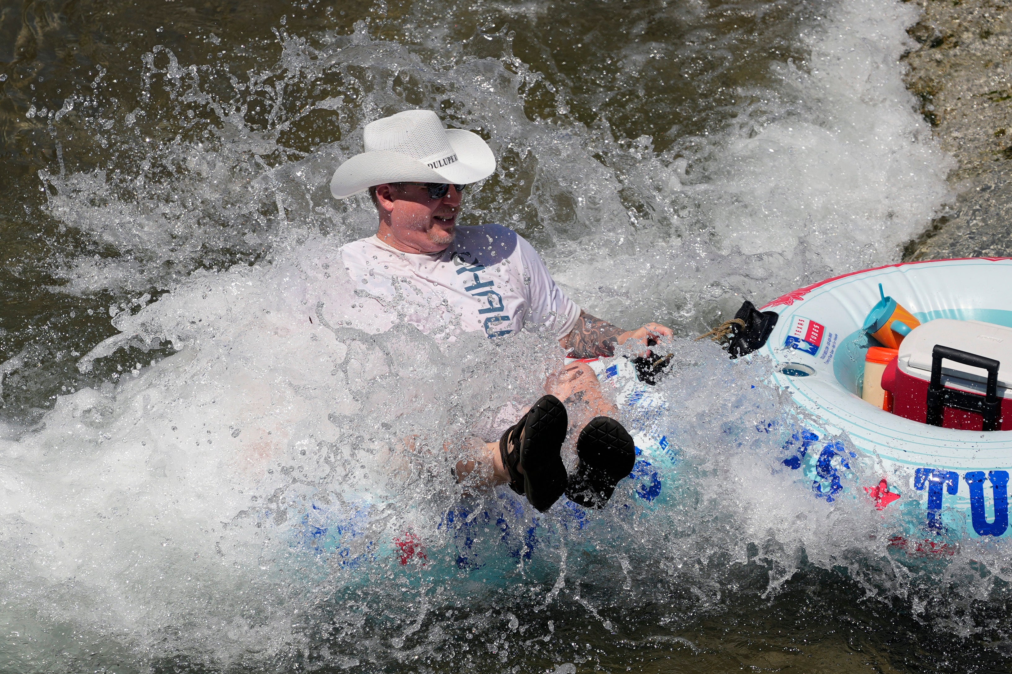 A tuber in a cowboy hat floats down Comal River on Wednesday in New Braunfels, Texas