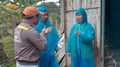 FAO Officials in blue coveralls talk to a Vietnamese farmer in front of a barn