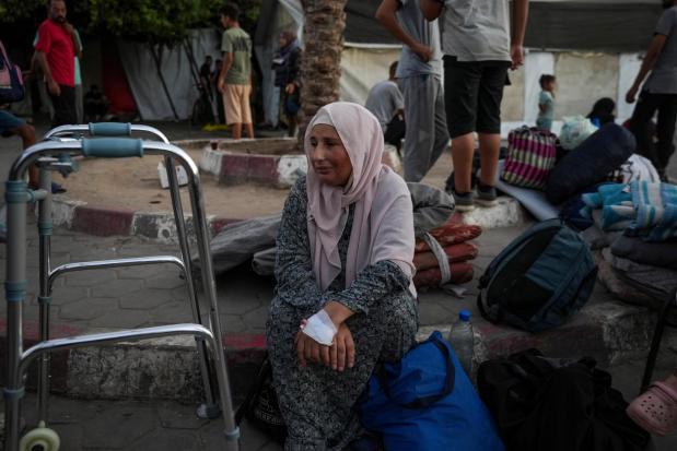 A woman sits on the curb next to her belongings outside the Al-Aqsa Martyrs Hospital in Deir al Balah, Gaza Strip, Sunday, Aug. 25, 2024. (AP Photo/Abdel Kareem Hana)