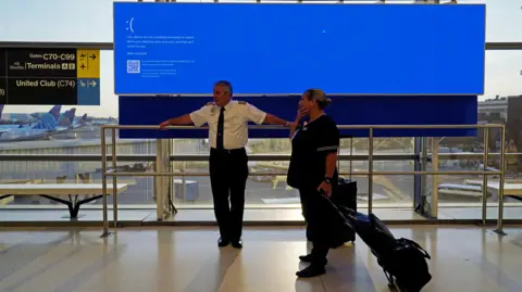 Reuters United Airlines employees wait by a departures monitor displaying a blue error screen.