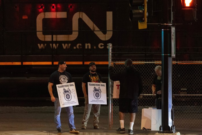 Two Teamsters union members hold picket signs at the entrance of a Canadian National rail yard in North Vancouver, British Columbia, Canada