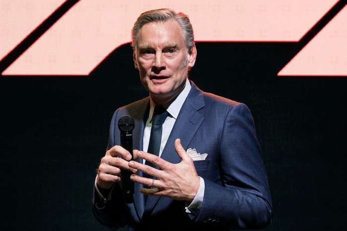 Sean Bratches speaks during a presentation of the 2018 season Renault Formula One at a Renault showroom in Paris. He is holding a microphone and wearing a navy blue suit with a white pocket square