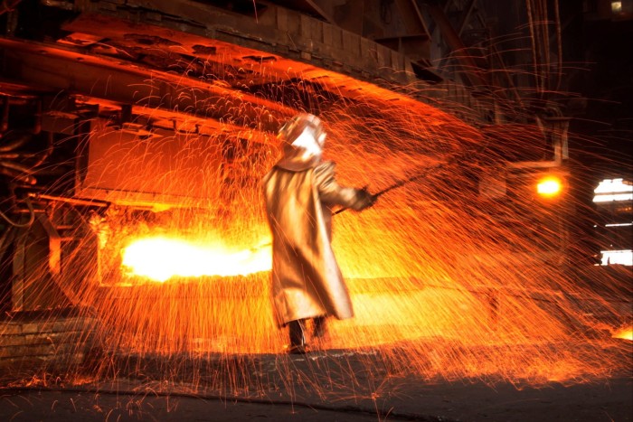 A worker in fireproof protective clothes processes nickel against a backdrop of sparks