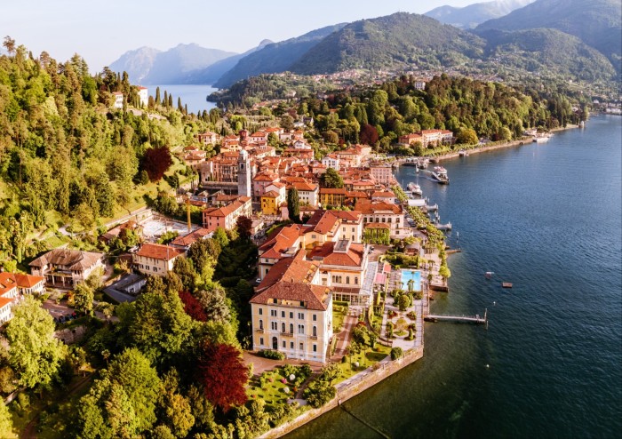 Aerial shot of terracotta-hued town by lake, with more water and mountains glimpsed behind