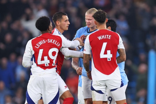 Arsenal players Lewis-Skelly and Ben White approach Erling Haaland on the football pitch.