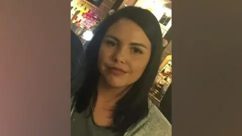 Family handout  Alice Webb is smiling at the camera, she has dark hair and a piercing in her lower lip. She stands in front of an illuminated bar.