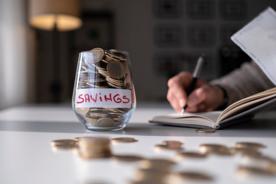 The man hand is putting a coin in a glass bottle and a pile of coins