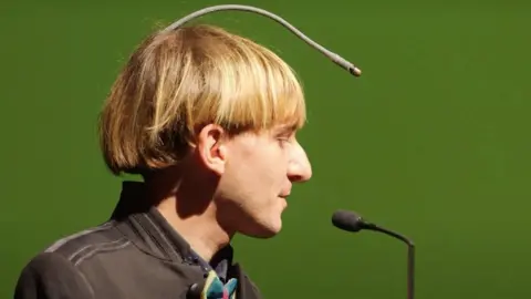 First Born Films Neil Harbisson side view of him and his antenna, which starts at the back of his head and goes in an arc to above his forehead