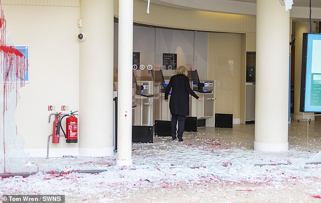 A woman in Bristol carefully picks her way over the shattered and stained broken window glass of a Barclays branch