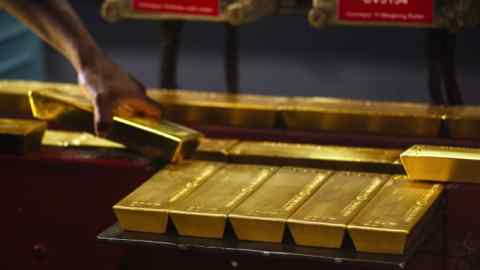 A worker lifts a gold bullion bar from a conveyor machine in South Africa