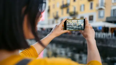 Getty Images A woman holding her phone in front of her so she can film a canal in Milan