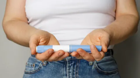 Getty Images Woman holding an obesity injection product