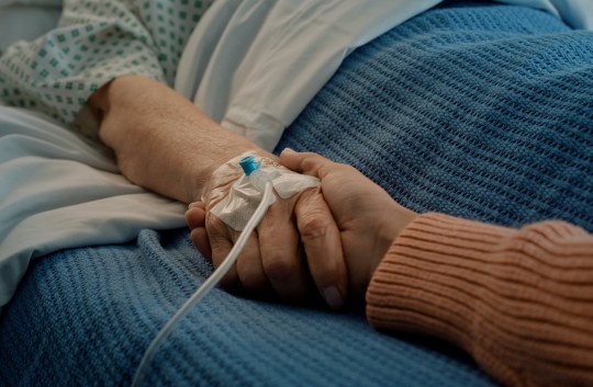 Hospital, holding hands and bed with hope, support and care together in a clinic after surgery. Senior, healthcare and cancer patient with empathy, kindness and caregiver with compassion with help