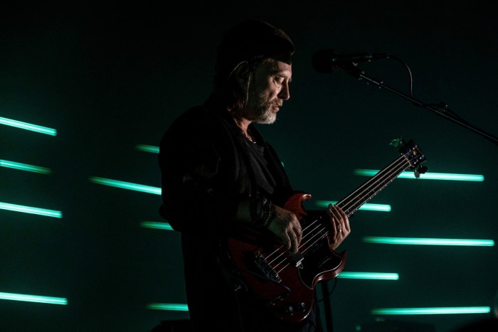 Thom Yorke is playing guitar on a dark stage. Behind him are some green strip lights