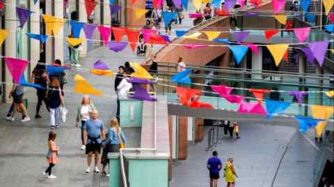 People walk through the Liverpool One shopping centre. The area is decorated with colorful triangular flags